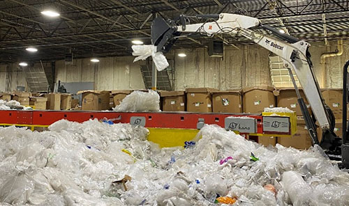 An excavator moves recycled plastic bags that are destined to be repurposed and used in AZEK Building Products in a warehouse